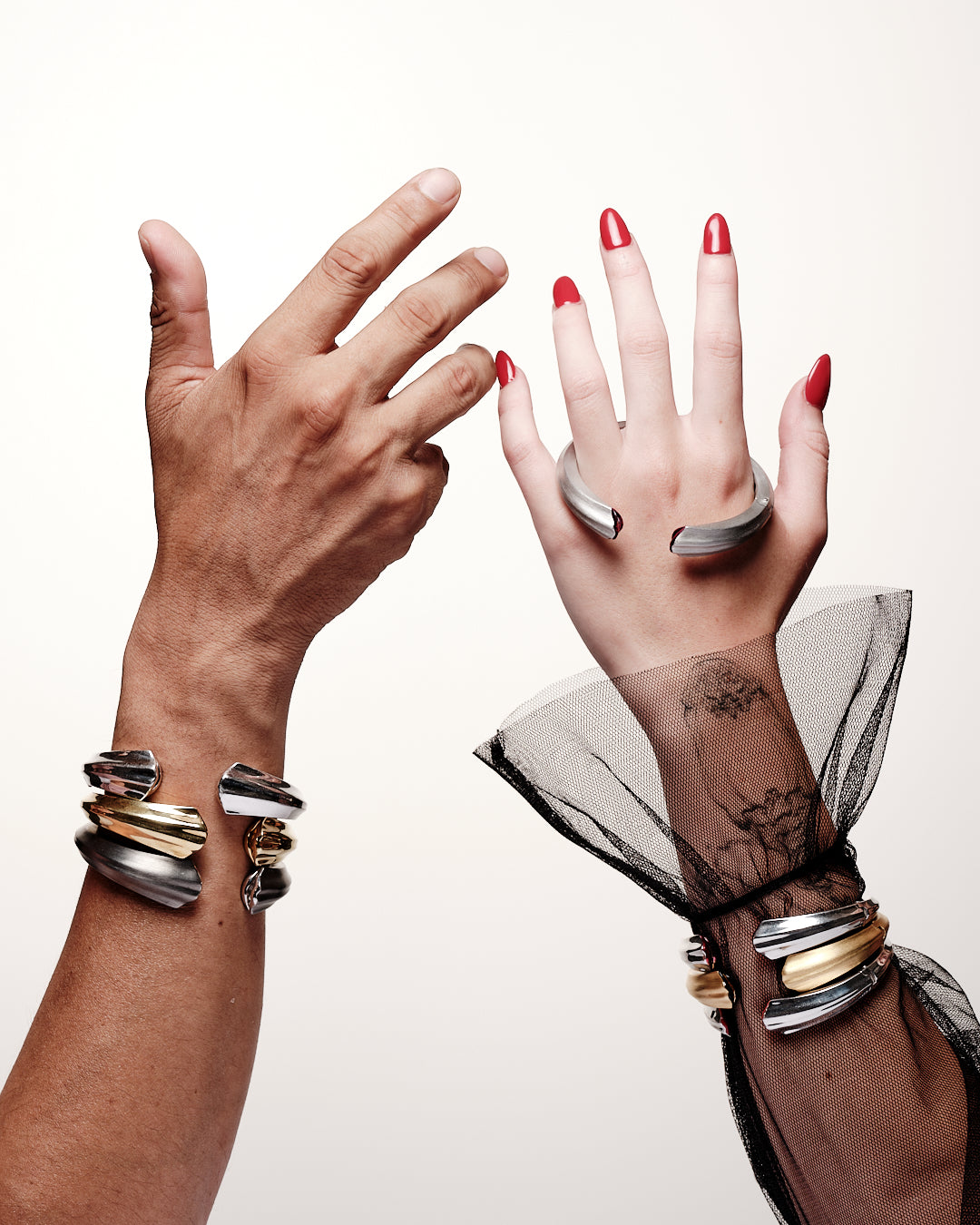Two hands with multiple bracelets and rings on a white background wearing fine jewelery 